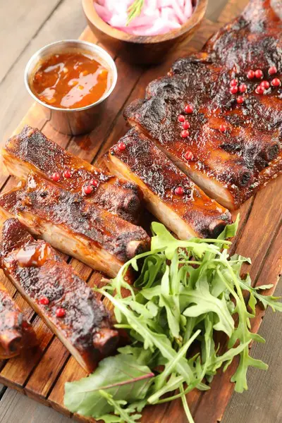 Lezzetli domuz pirzolası, roka, sos ve soğan ahşap masada, üst tarafta.