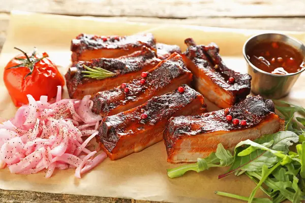 Lezzetli domuz kaburgası, sos, roka ve soğan ahşap masada, yakın plan.