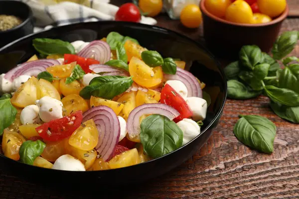 Sarı domatesli lezzetli salata, fesleğen, soğan ve ahşap masada mozzarella peyniri, yakın plan.