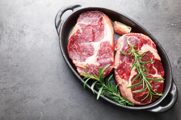 Çiğ et ve baharat parçaları gri desenli masa üzerinde fırın kabında, üst manzara. Metin için boşluk