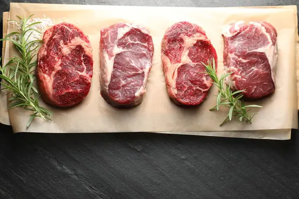 Çiğ et parçaları, biberiye ve tuz siyah masada, üst görünümde.