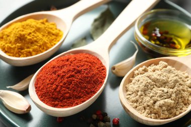 Gri masadaki kaşıklardaki farklı baharatlar, yakın plan.