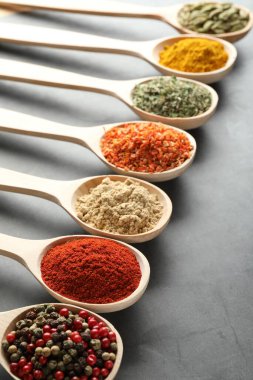 Gri masadaki kaşıklardaki farklı baharatlar, yakın plan.