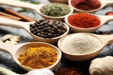 Siyah masadaki kaşıklardaki farklı baharatlar, yakın plan.