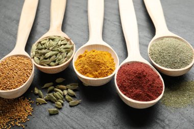 Siyah masada kaşıklardaki farklı aromatik baharatlar, yakın plan.