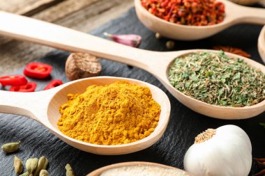 Tahta masadaki kaşıklardaki farklı aromatik baharatlar, yakın plan.