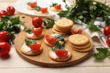 Krem peynirli krakerler, domatesler ve maydanozlar beyaz ahşap masada, yakın plan.