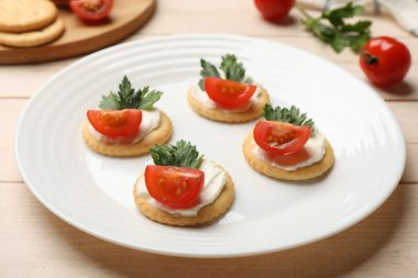 Krem peynirli krakerler, domatesler ve maydanozlar beyaz ahşap masada, yakın plan.