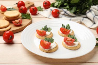 Krem peynirli krakerler, domatesler ve maydanozlar beyaz ahşap masada, yakın plan.