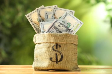 Dolar işaretli para çantası ve ahşap masa üzerindeki banknotlar bulanık yeşil arka plan, yakın plan
