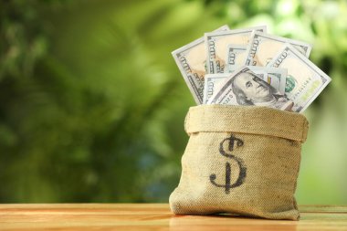 Dolar işaretli para çantası ve ahşap masanın üzerindeki banknotlarla bulanık yeşil arka plan, yakın plan. Metin için boşluk