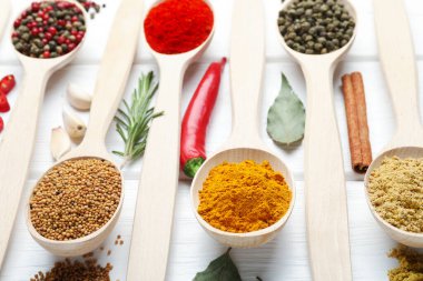 Beyaz ahşap masadaki kaşıklarda farklı aromatik baharatlar, yakın plan.