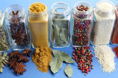 Mavi arka planda kavanozlardaki farklı aromatik baharatlar, yakın plan.