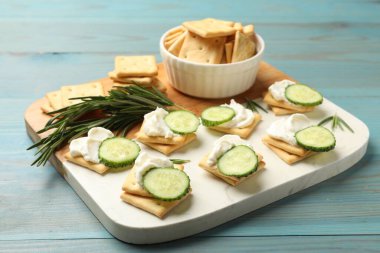 Krem peynirli krakerler, biberiye ve salatalık açık mavi ahşap masada, yakın plan.