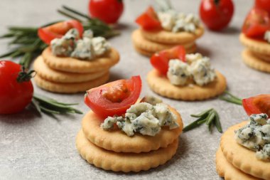 Lezzetli krakerler mavi peynirli, biberiyeli ve domatesli gri desenli masa, yakın plan.