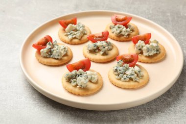 Lezzetli krakerler, mavi peynirli ve domatesli gri desenli masa, yakın plan.