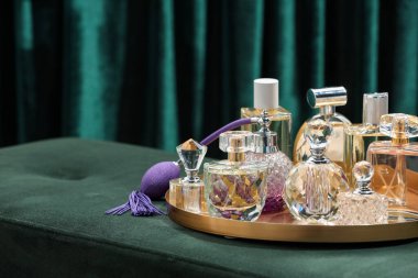 Yeşil pouf 'ta, deniz mavisi perdelerin yanında farklı lüks parfümler, yakın plan. Metin için boşluk
