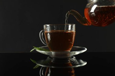 Koyu ayna masasında çaydanlıktan fincana taze demlenmiş çay dökülüyor.