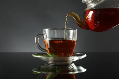 Koyu ayna masasında çaydanlıktan fincana taze demlenmiş çay dökülüyor.