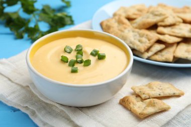 Lezzetli peynir sosu kaseye, krakerler açık mavi masaya, yakın plan.