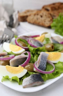 Ringa balıklı lezzetli salata, yumurta ve sebzeler beyaz masada, yakın plan.