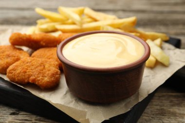 Tabakta nefis peynir sosu, tavuk nugget ve ahşap masada patates kızartması, yakın plan.