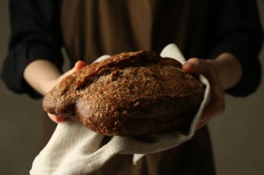 Gri arka planda taze ekmek somunu olan kadın, yakın plan.