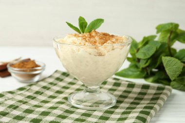 Tarçınlı lezzetli pirinç pudingi ve beyaz masadaki cam tatlı kasesinde naneli şeker.