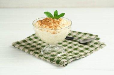 Tarçınlı lezzetli sütlaç, beyaz ahşap masada nane ve kaşık, yakın plan.