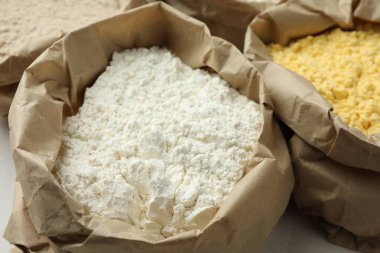 Beyaz masadaki kağıt torbalarda farklı türde un, yakın plan.