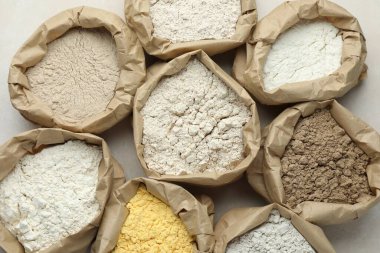 Beyaz masadaki kağıt torbalarda farklı türde un, düz yerde.