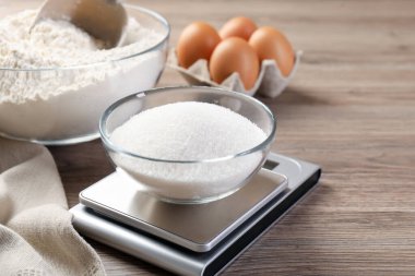 Dijital mutfak terazisi, bir kase şeker ve ahşap masa üzerindeki diğer ürünler, yakın plan.