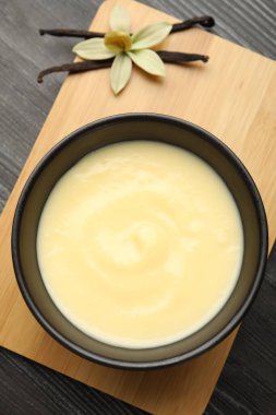 Lezzetli vanilyalı puding kasede, çiçek ve kapsüller ahşap masada, üst manzara