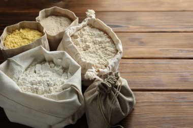 Tahta masadaki poşetlerdeki farklı un türleri, yakın plan. Metin için boşluk