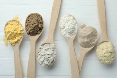 Beyaz ahşap masadaki kaşıklarda farklı türde un, düz.