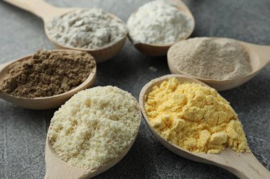 Gri masadaki kaşıklarda farklı türde un, yakın plan.