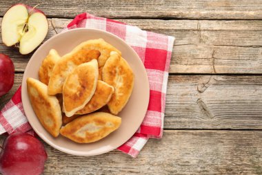 Lezzetli kızarmış pirizky (doldurulmuş turtalar) ve ahşap masa üzerinde elmalar, düz yatak. Metin için boşluk