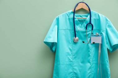 Steteskop ve rozeti açık yeşil arka planda asılı sağlık görevlisi üniforması. Metin için boşluk