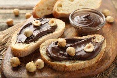 Çikolata sürülmüş ekmek dilimleri ve ahşap masada fındıklar, yakın plan.