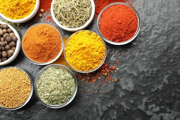 Tabaklardaki farklı aromatik baharatlar karanlık masada, düz yerde. Metin için boşluk