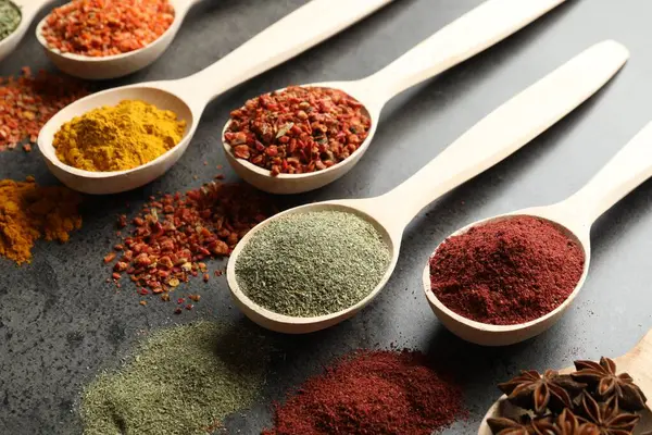 Gri masadaki kaşıklardaki farklı baharatlar, yakın plan.