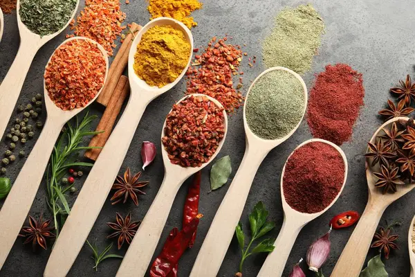 Gri masadaki kaşıklardaki farklı baharatlar düzdü.