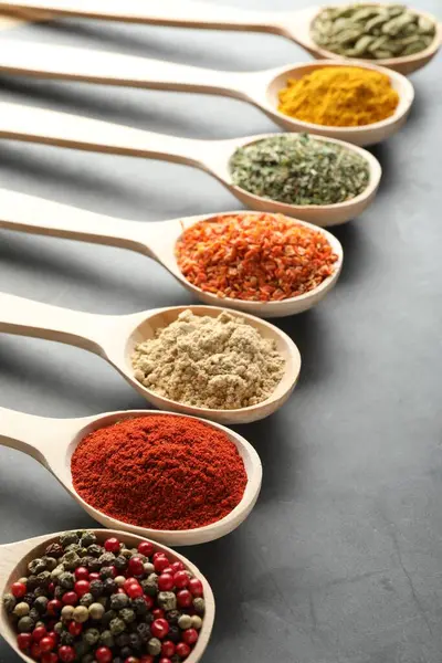 Gri masadaki kaşıklardaki farklı baharatlar, yakın plan.