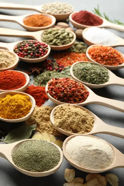 Gri masadaki kaşıklardaki farklı baharatlar, yakın plan.