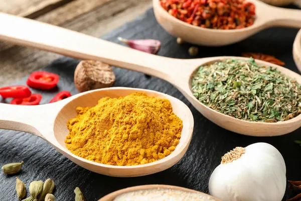 Tahta masadaki kaşıklardaki farklı aromatik baharatlar, yakın plan.