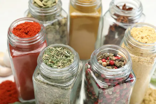 Beyaz masadaki kavanozlarda farklı aromatik baharatlar, yakın plan.