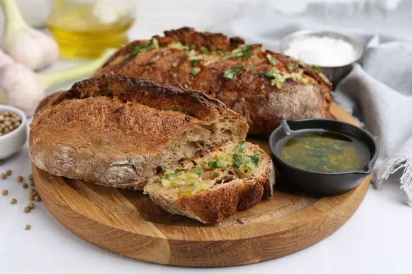 Sarımsaklı lezzetli ekmek, otlar ve yağlı beyaz fayanslı masa, yakın çekim.