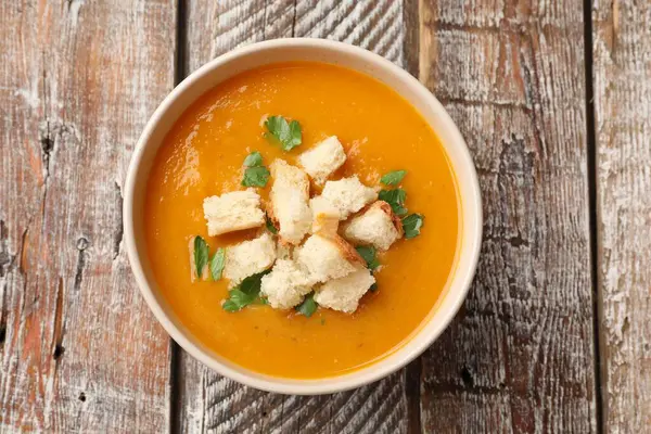 Lezzetli balkabağı kremalı çorba, kızarmış ekmek ve ahşap masada maydanoz.