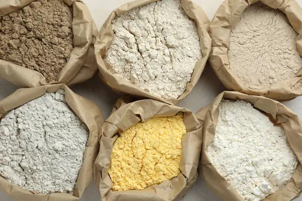 Beyaz masadaki kağıt torbalarda farklı türde un, düz yerde.