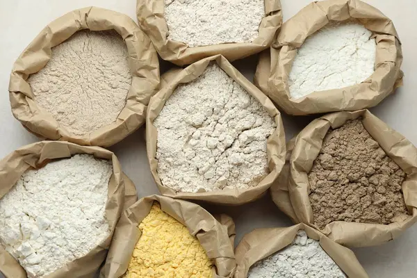 Beyaz masadaki kağıt torbalarda farklı türde un, düz yerde.